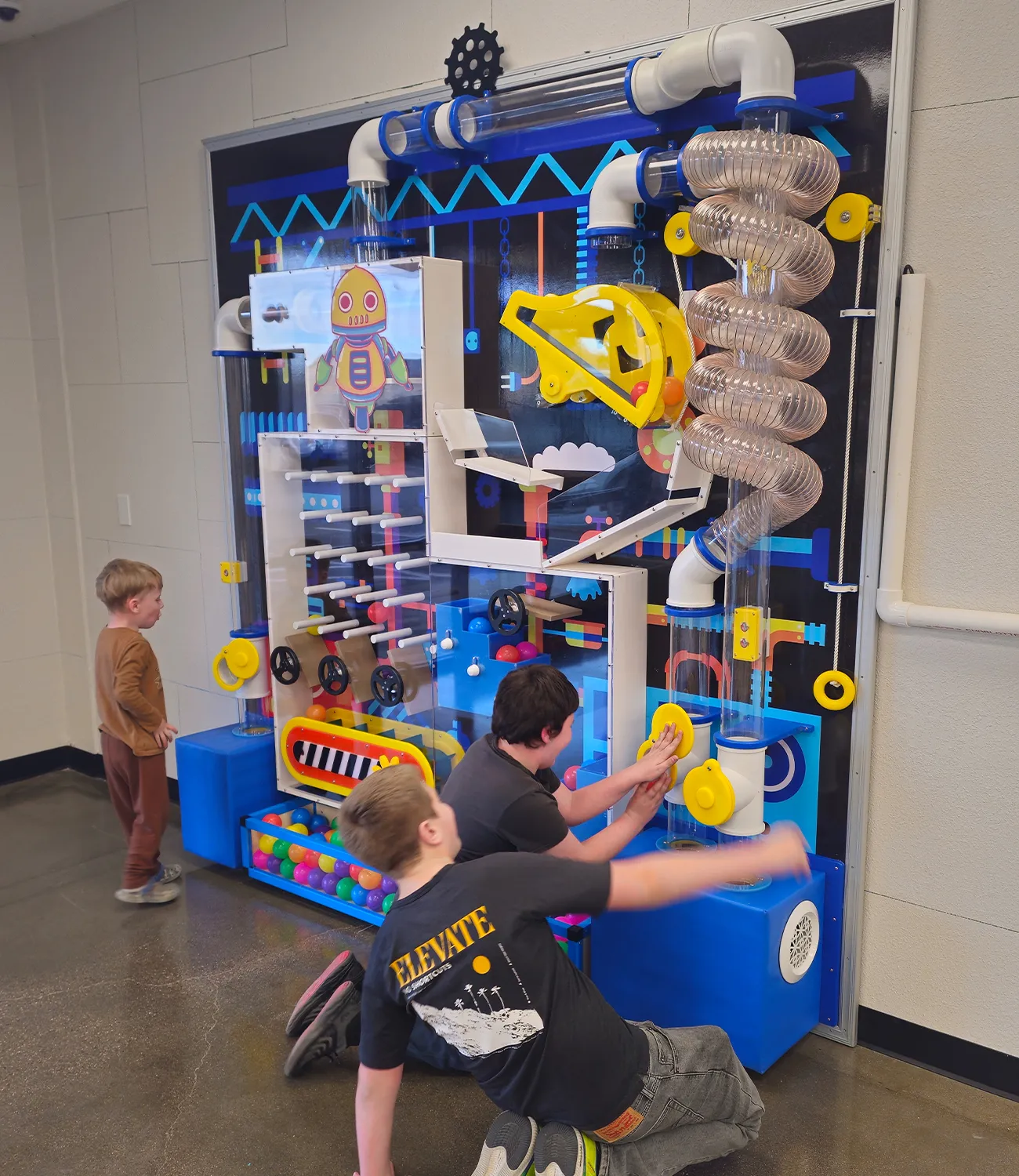 air-launcher-1 | LiteZilla Kids interact with a large colorful hands-on science wall featuring tubes, gears, and levers.