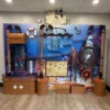 Colorful pirate/treasure-themed indoor play wall for kids, with tubes, a life preserver, a steering wheel, and treasure chests set against a blue mural.