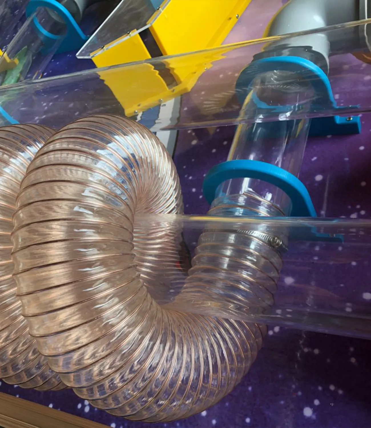 ball-launcher-4 | LiteZilla Coiled flexible metal duct attached to a clear plastic tube with blue circular clamps inside a colorful machine.
