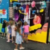 Kids gather around a bright space-themed interactive wall with colorful plastic pipes and levers, like a marble maze on a black space backdrop.