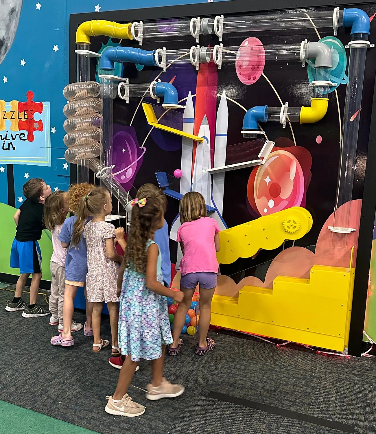 ball-launcher-8 | LiteZilla Kids gather around a bright space-themed interactive wall with colorful plastic pipes and levers, like a marble maze on a black space backdrop.