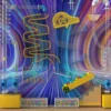Vivid abstract playground wall with a yellow winding slide and assorted tubes against a rainbow striped background.