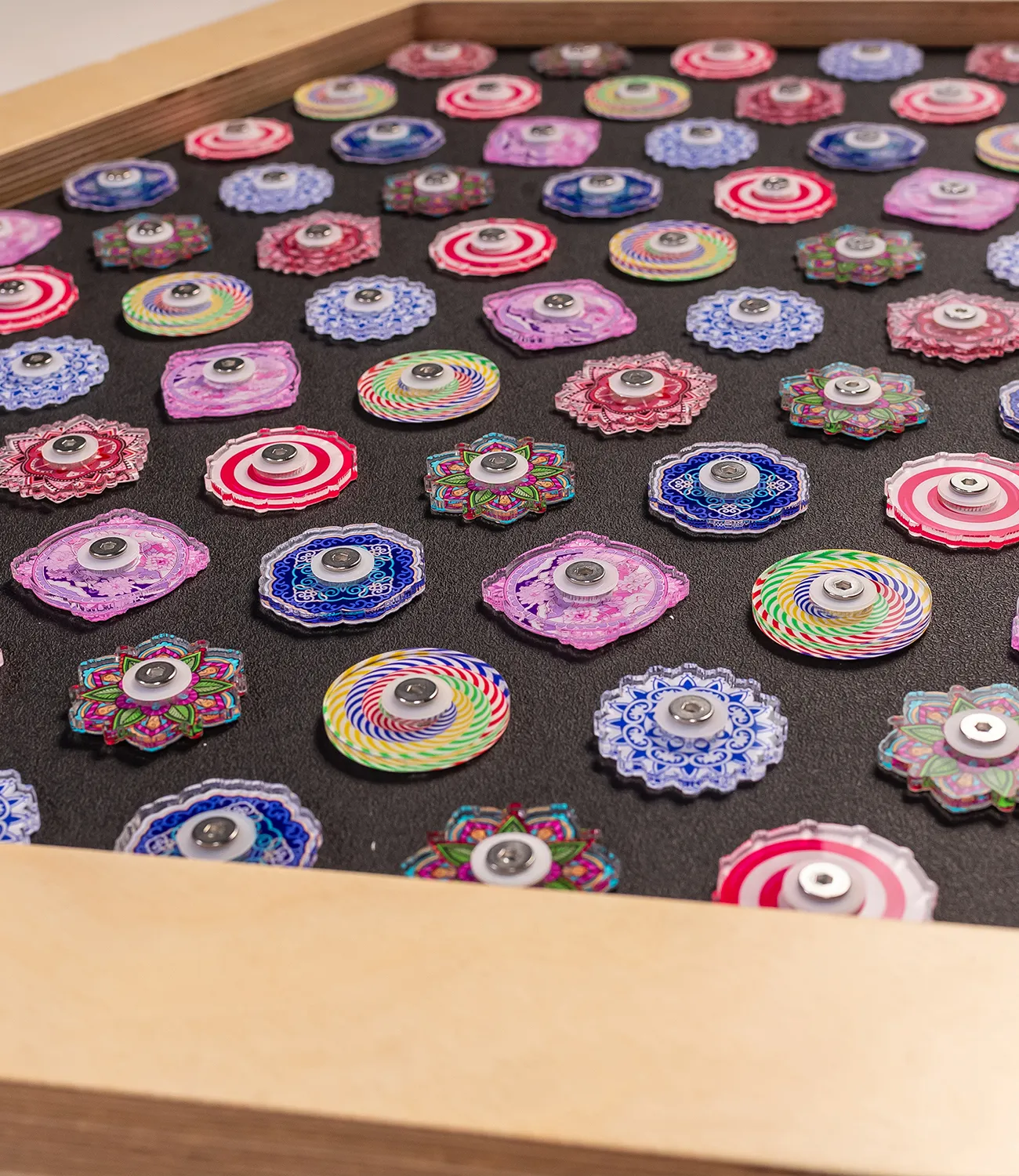 fidget-spinner-small 1 | LiteZilla Collection of colorful, patterned spinning tops laid out on a black surface inside a wooden box.