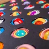 Colorful swirled lollipops resting in a black baking tray with circular holes.