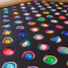 Close-up of a wooden-framed tray with a black foam insert filled with colorful layered spheres in evenly spaced circular holes.