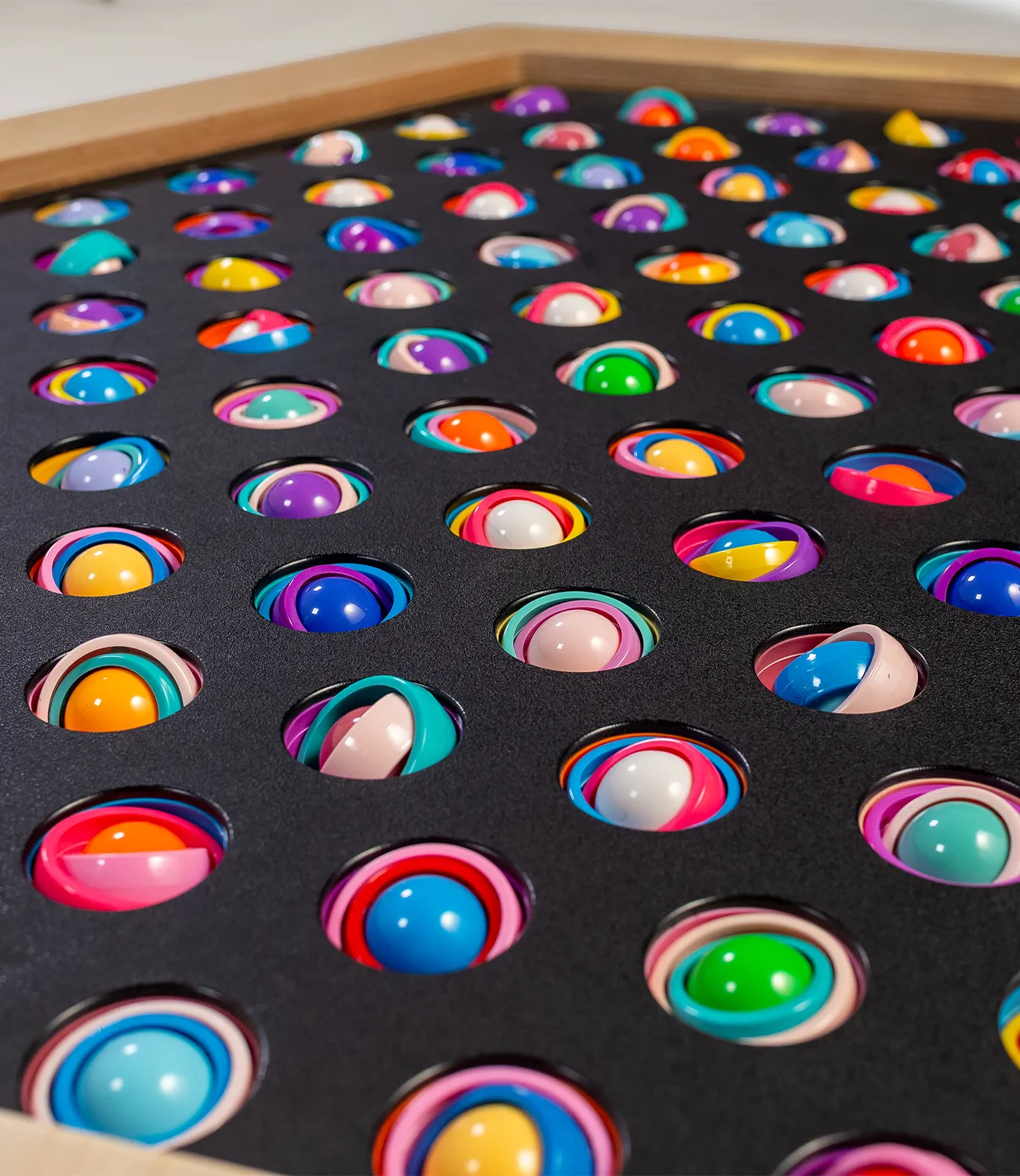 gyro-rings-2 | LiteZilla Close-up of a wooden-framed tray with a black foam insert filled with colorful layered spheres in evenly spaced circular holes.